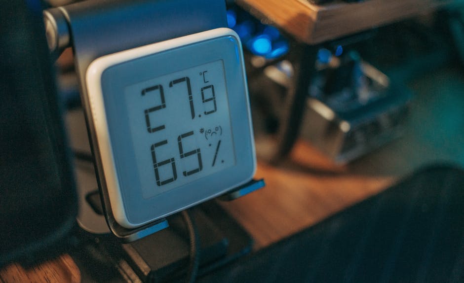 Rankoje laikomas skaitmeninis higrometras ant stalo, rodomi drėgmės procentai